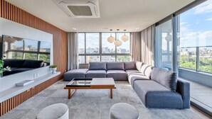 A modern living room with a large sectional sofa, a flat-screen TV mounted on the wall, and a city view through large windows. - JP Redenção, Unique Studio at Downtown Porto Alegre (Farroupilha Porto Alegre)