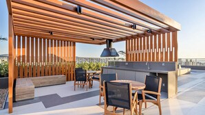 An outdoor patio with wooden furniture, a grill, and a view of the city. - JP Redenção, Unique Studio at Downtown Porto Alegre (Farroupilha Porto Alegre)