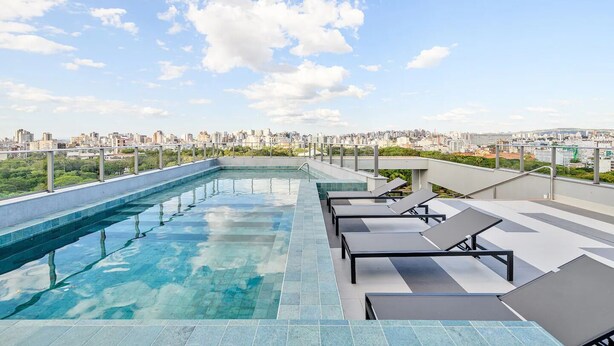 A rooftop pool with clear blue water, surrounded by lounge chairs and a cityscape view. - JP Redenção, Unique Studio at Downtown Porto Alegre (Farroupilha Porto Alegre)