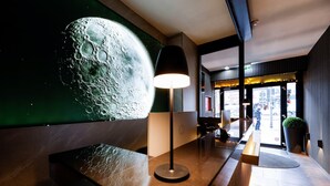 Un espace d’accueil agrémenté d’une grande fresque représentant la lune, d’une lampe moderne, d’un comptoir de réception et offrant une vue sur la rue.