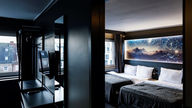 Une chambre d’hôtel avec une grande fenêtre, un bureau avec un ordinateur et deux lits.