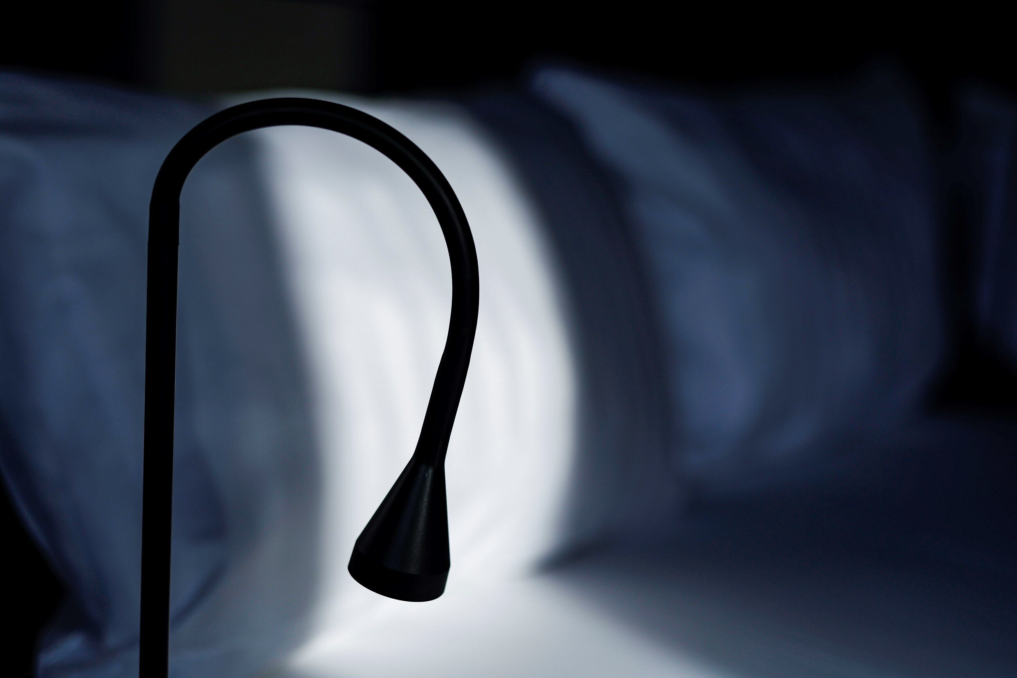 A single black lamp with a curved neck on a bed.