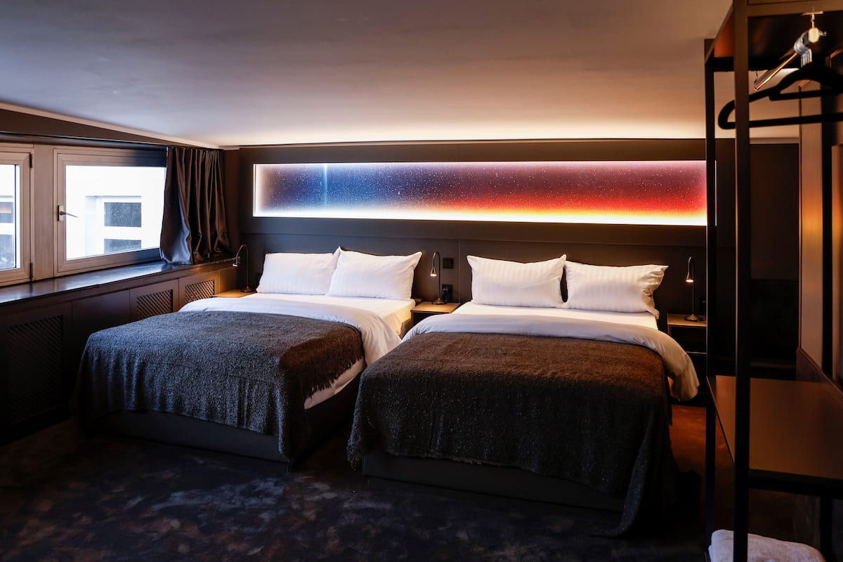 A hotel room with two beds, a large window, and a wall-mounted light fixture.