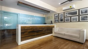 A reception area with a wooden reception desk, a white sofa, and a wall with framed black and white photos. - Treebo Cool River (Visakhapatnam)