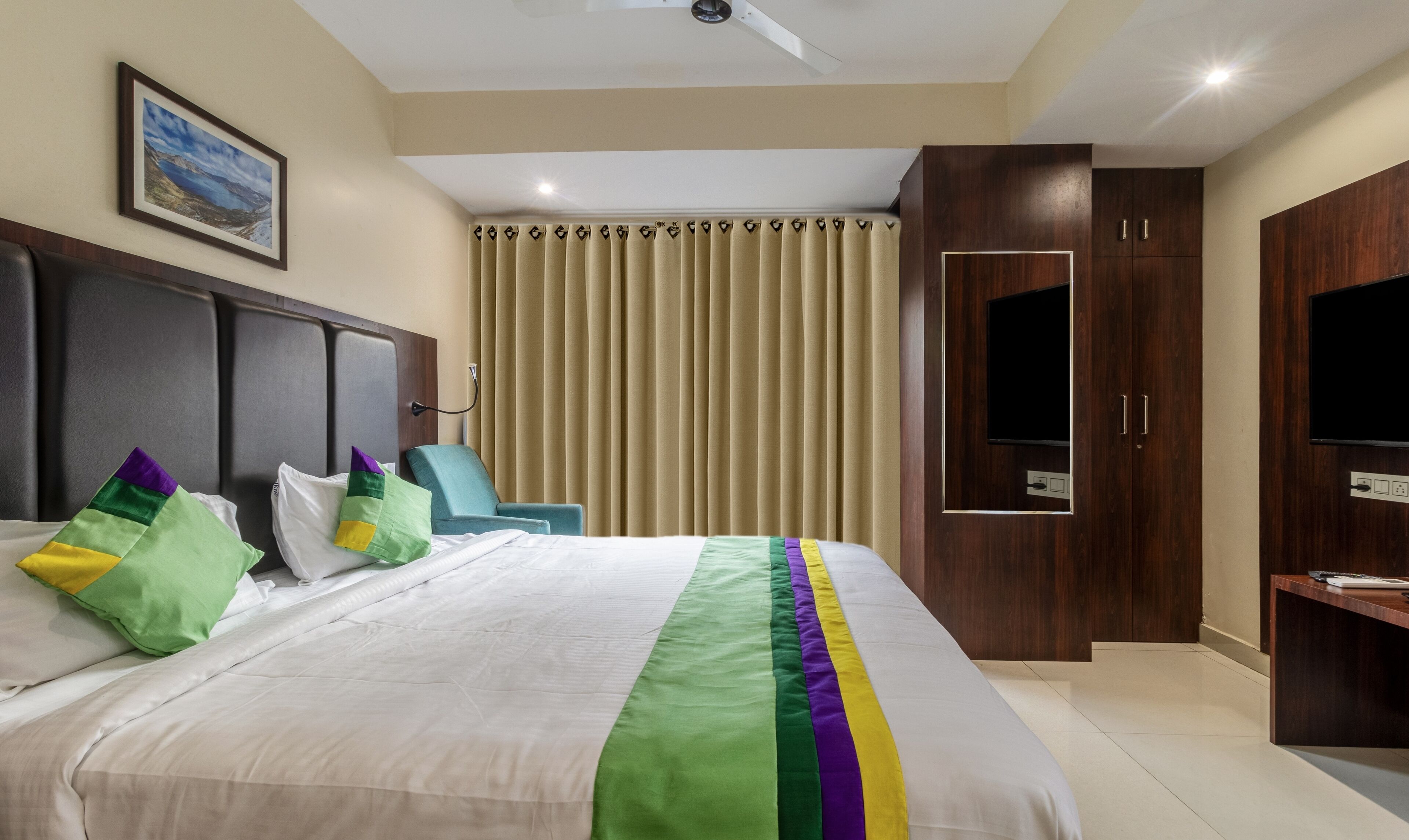 A hotel room with a large bed, a television, a wardrobe, and a window with curtains.