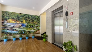 A lobby with a mural of a temple complex, a marble wall, a fire alarm, and several potted plants. - Treebo Cool River (Visakhapatnam)