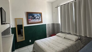 Une chambre à coucher avec un lit, une télévision, un miroir et une fenêtre avec des rideaux.
