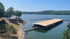 A docked boat with a covered area, a swimming pool, and a forested shoreline. - Osage Beach Condo getaway! (Osage Beach)