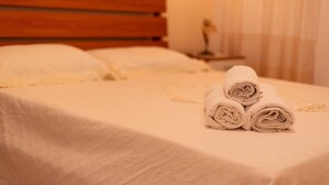 Uma cama bem arrumada com cabeceira de madeira, roupa de cama branca e toalhas enroladas sobre a cama.
