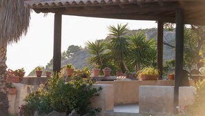 Área externa coberta com telhado de terracota, vasos com plantas e parede de pedra.