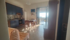 Cozinha com armários azuis, uma mesa de jantar com cadeiras e vista para o exterior por uma porta de vidro.