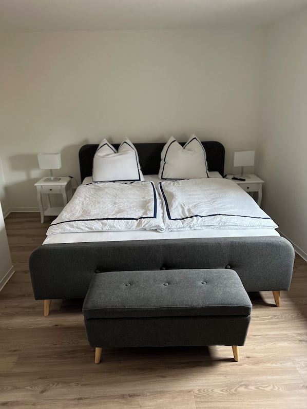 Un dormitorio con una cama grande, dos mesitas de noche y un taburete gris.