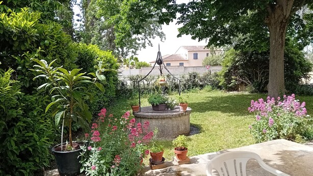 A garden with potted plants, a white plastic chair, and a concrete table. - Gite en Provence capacité 6 personnes (Entressen)