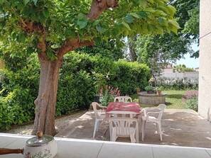 Eine Terrasse mit Tisch und Stühlen, umgeben von üppiger Vegetation und einem Baum.