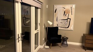 A room with a sliding glass door, a black chair, a small round table with a lamp, and a large abstract painting on the wall. - Brand New Luxurious and Modern Family House (Lucan)