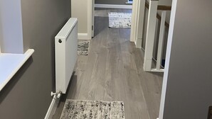 A hallway with a radiator, a patterned rug, and a staircase with wooden railings. - Brand New Luxurious and Modern Family House (Lucan)