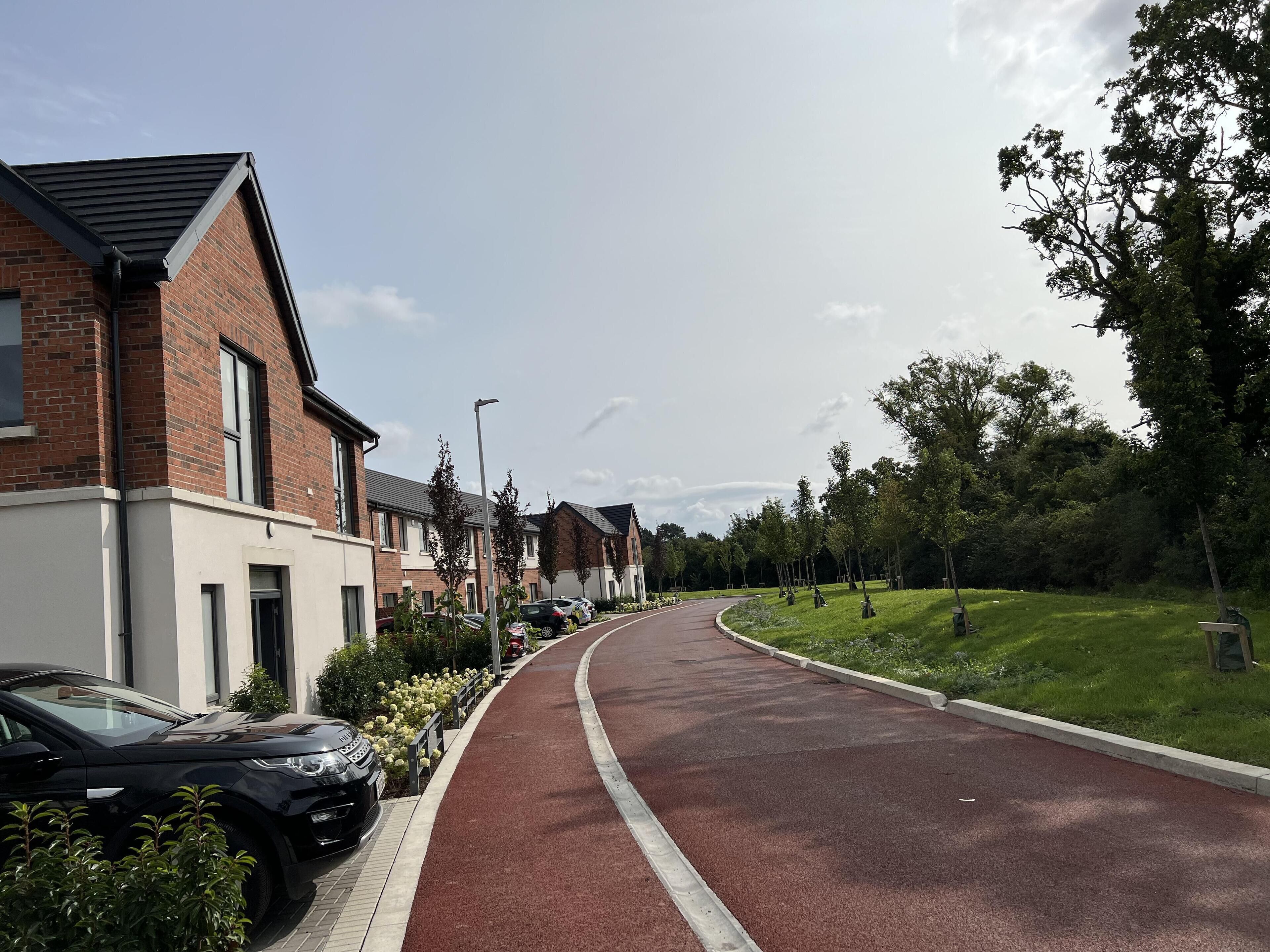 A residential street with houses, a red bike path, and parked cars.