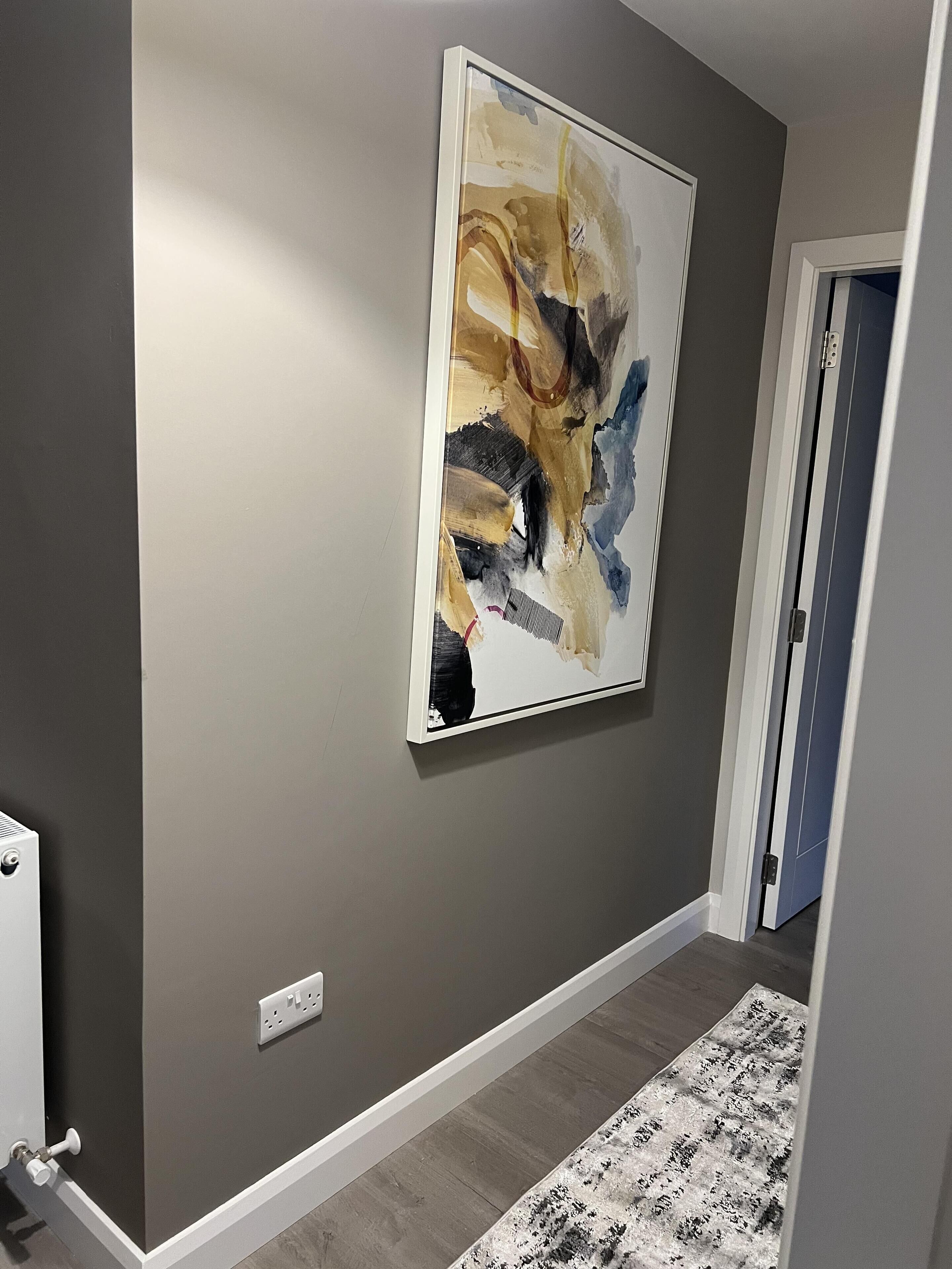A hallway with a gray wall, a large abstract painting, a patterned rug, and a door.
