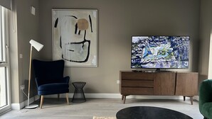 A modern living room with a large TV, abstract art, a blue chair, a green chair, and a wooden cabinet. - Brand New Luxurious and Modern Family House (Lucan)
