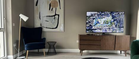 A modern living room with a large TV, abstract art, a blue chair, a green chair, and a wooden cabinet.