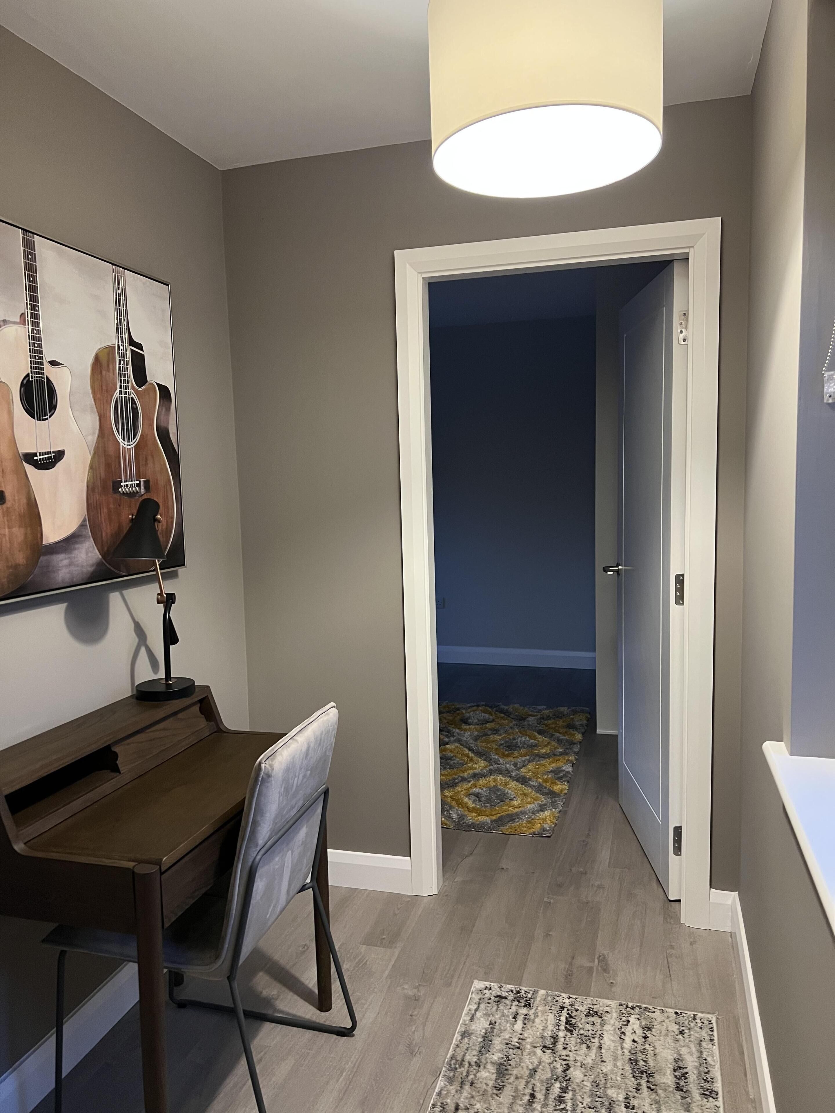A room with a desk, chair, and a painting of guitars on the wall.