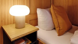 A wooden bedside table with a lamp, a white pillow, and a brown pillow on a bed. - homie stay radapartment (Iphofen)