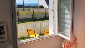 A bedroom with a bed, a window, and a view of the sea and houses. - Maison Refaite et Lumineuse, vue Mer, à 5 Minutes de la Plage (Plogoff)