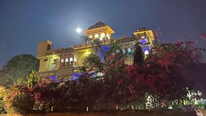 A large, illuminated building with a prominent dome and two smaller domes, surrounded by lush greenery and flowering plants. - Deogarh Hills A Village Experience Property (Deogarh Madaria)