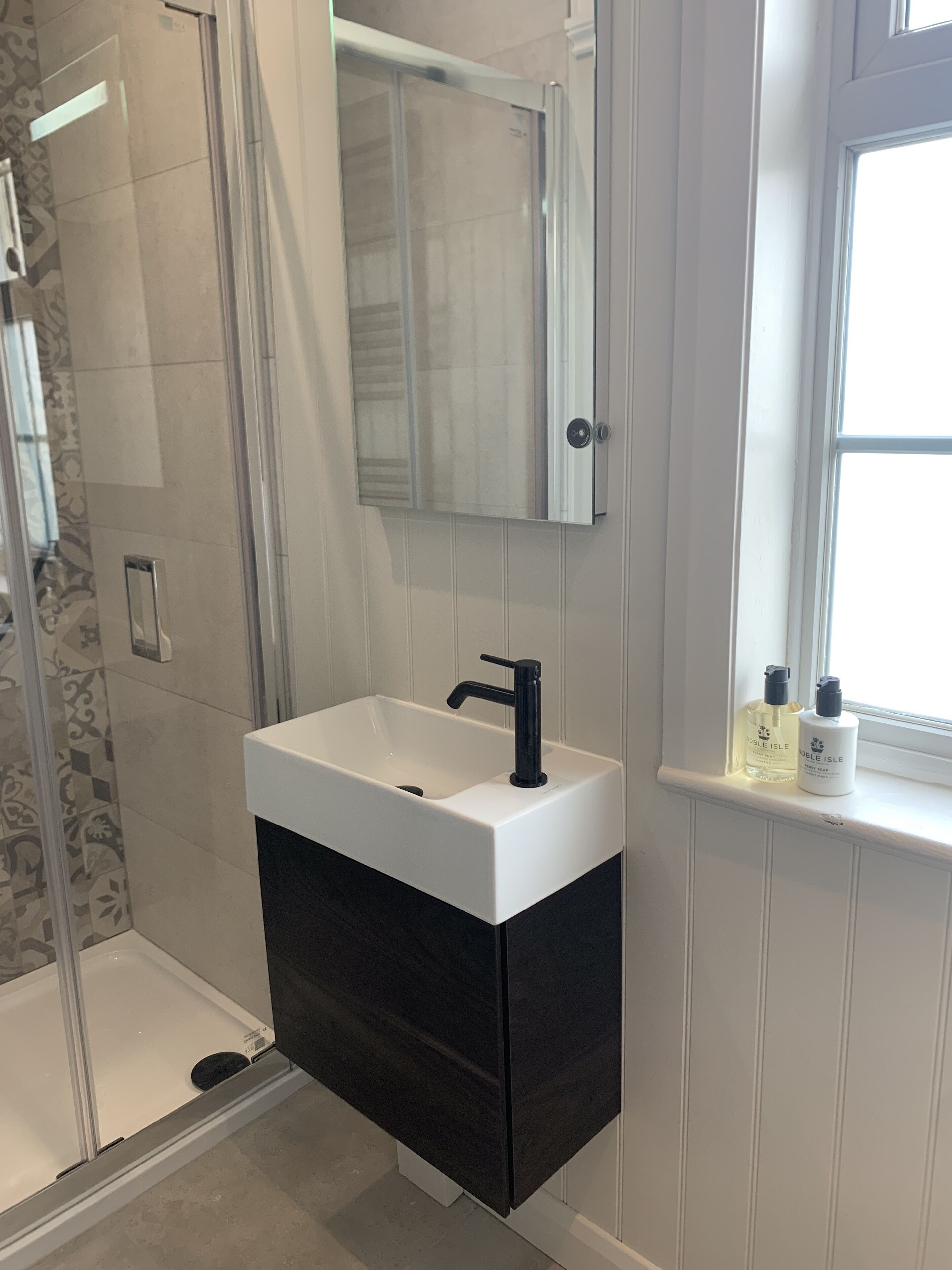 Un bagno con lavandino bianco, mobile contenitore nero e finestra vista.
