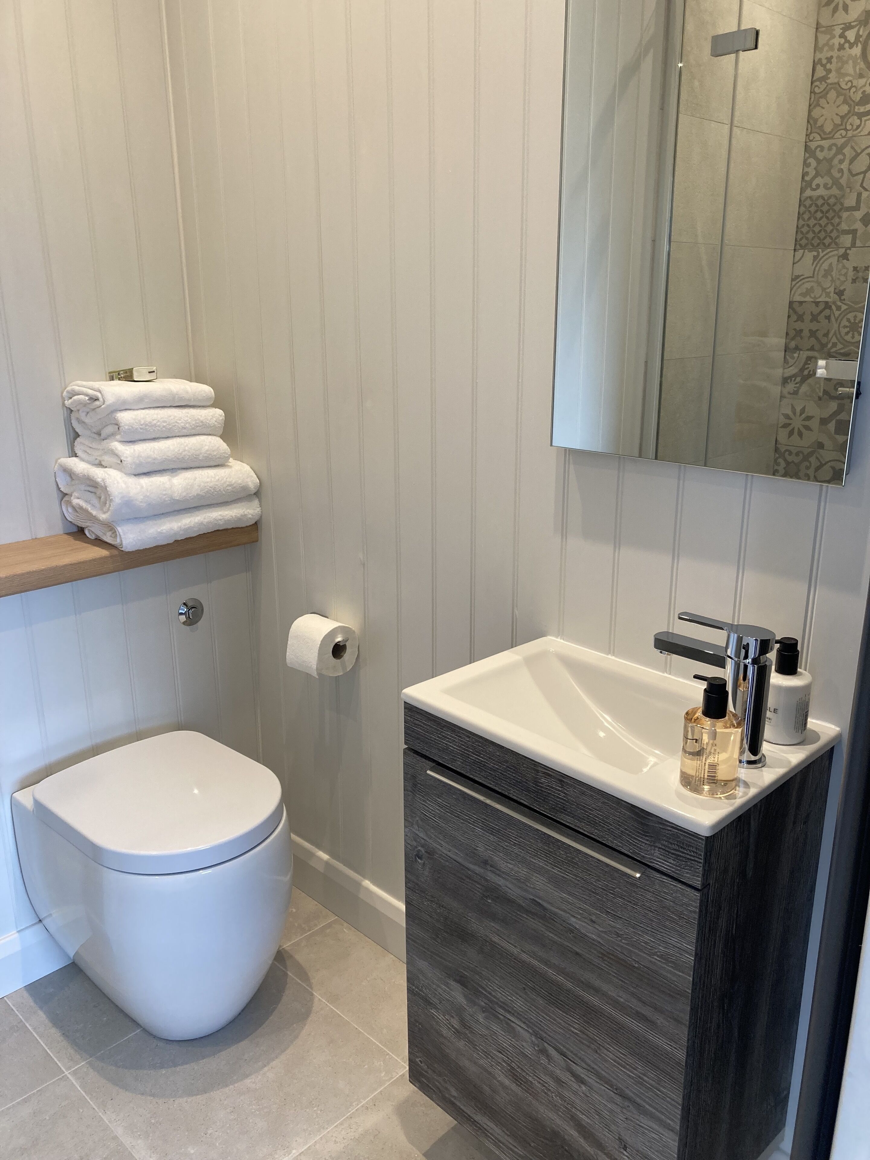 Un baño moderno con inodoro, lavamanos con espejo y un perchero para toallas.