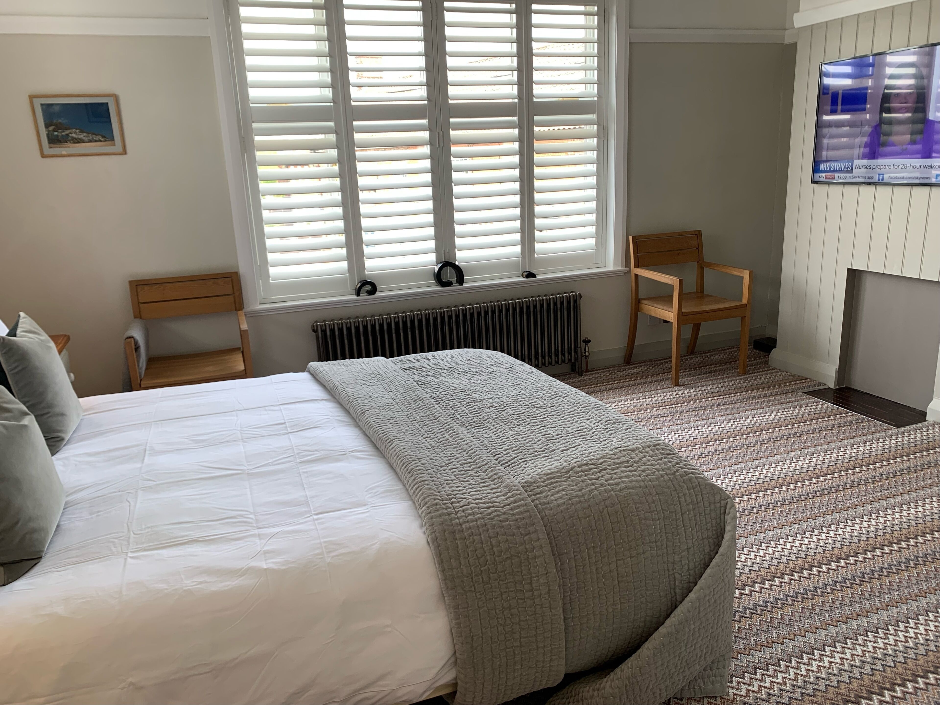 A bedroom with a large bed, a chair, a radiator, and a TV on the wall.