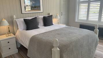 A neatly arranged bedroom with a bed, bedside lamps, a framed picture on the wall, and a window with blinds.