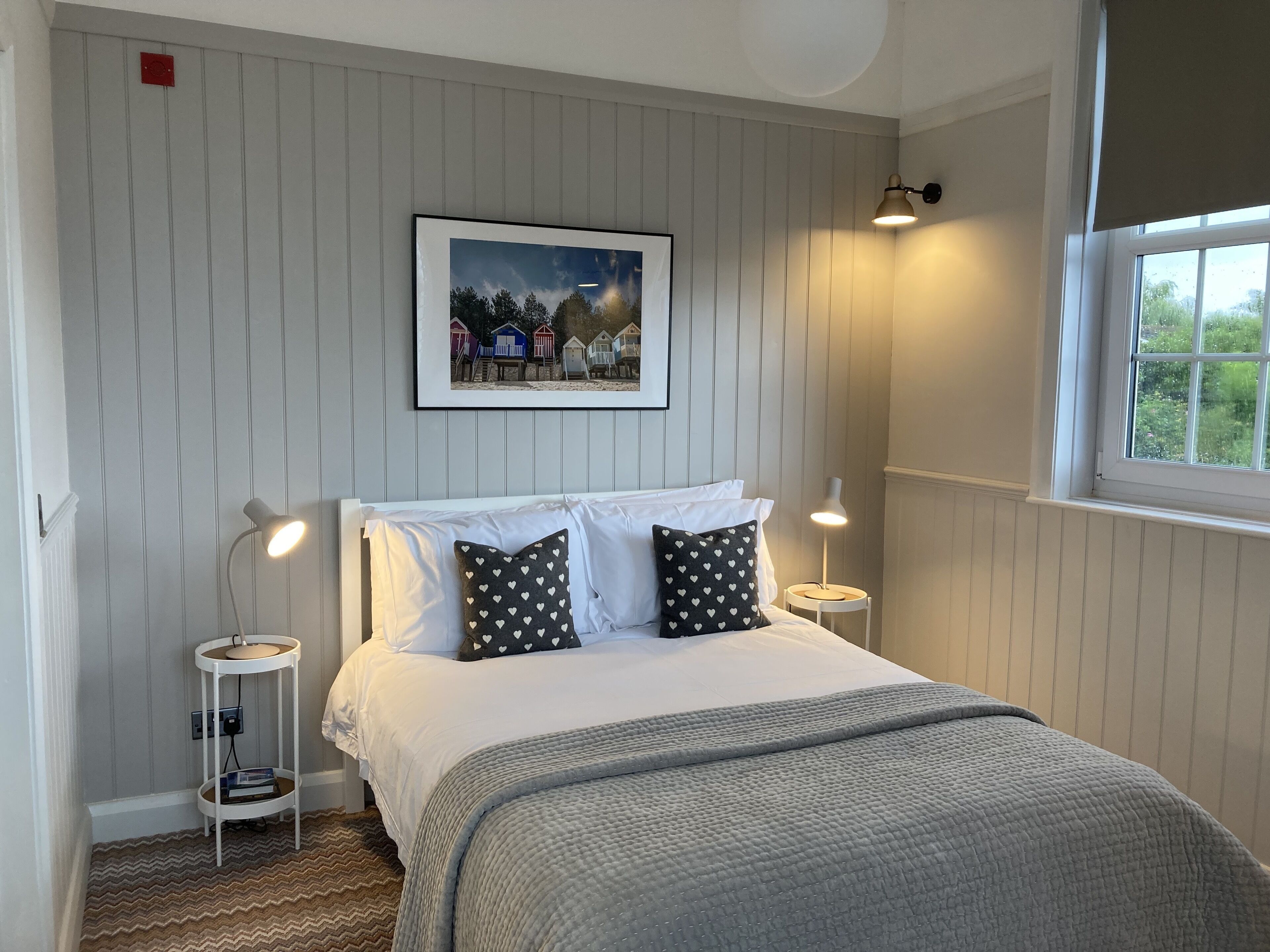 Une chambre à coucher bien rangée, avec un lit, deux tables de chevet, un tableau encadré au mur et une fenêtre donnant sur un paysage agréable.