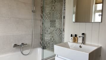 A bathroom with a bathtub, shower, and a sink with a mirror above it.
