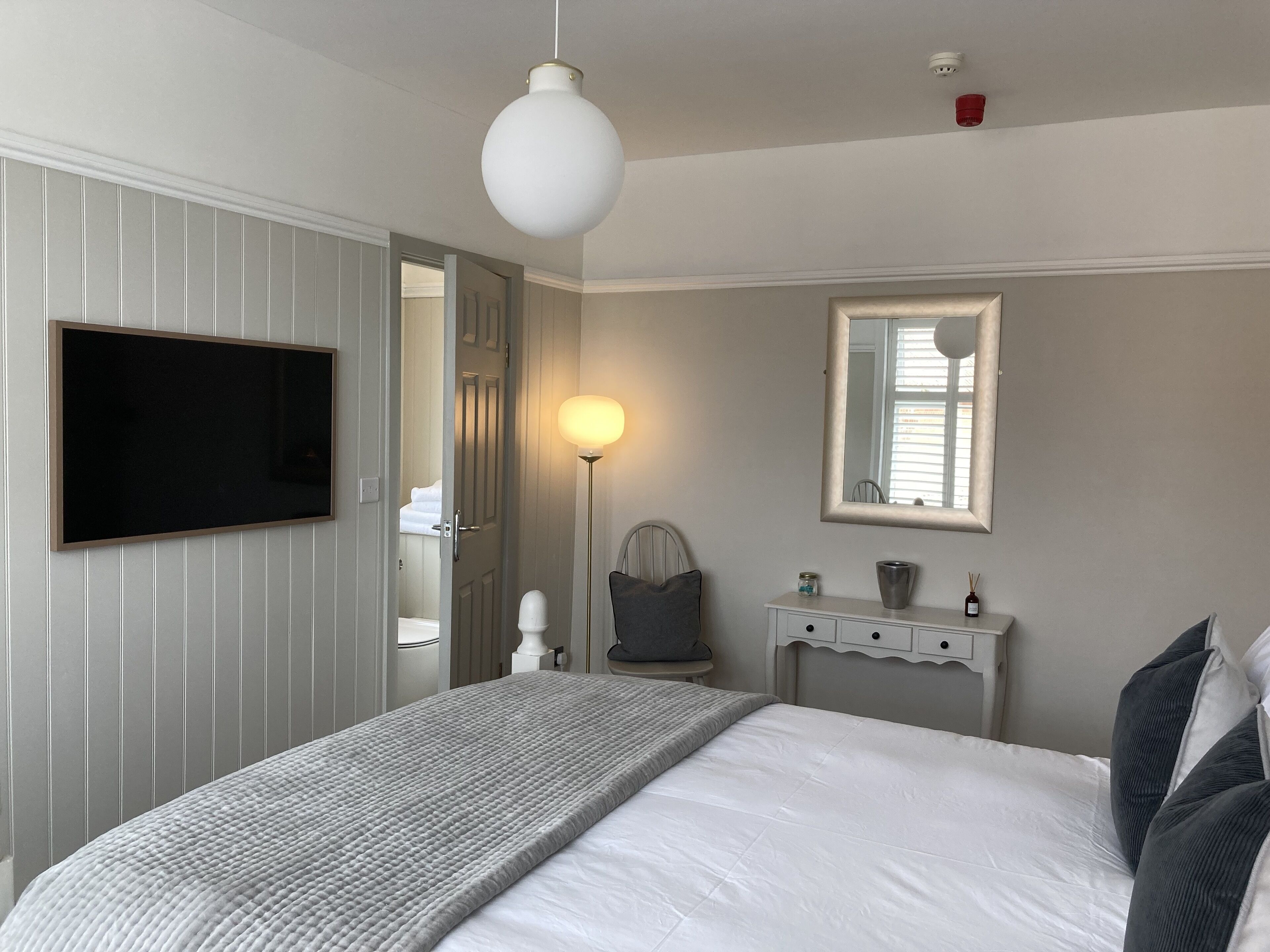 Un dormitorio con cama, mesita de noche, espejo, televisor de pantalla plana y una puerta que da a otra habitación.