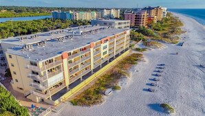 Un hotel de varios pisos con balcones, situado junto a una playa con sombrillas y un sendero de arena.