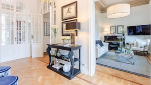 Een ruime woonkamer met een piano, een witte bank en een kroonluchter.