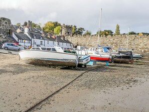 A beach with boats moored in the sand, a stone wall, and buildings in the background.