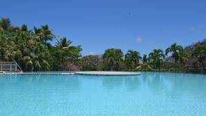 A clear blue swimming pool surrounded by palm trees and a white fence. - Ti Cocon de Standing (Saint-François)
