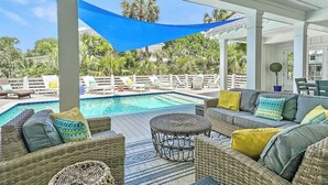 A covered outdoor area with a pool, wicker furniture, and a blue shade sail.