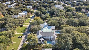 An aerial view of a residential area with houses, a swimming pool, and a beach in the background.