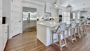 A modern kitchen with white cabinetry, a stainless steel refrigerator, and a large island with bar stools.