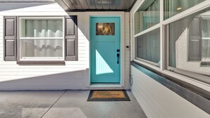 Une porte turquoise avec un paillasson, une fenêtre avec des stores et une façade en bois.