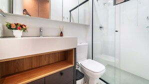 Un baño moderno con cabina de ducha de vidrio, un lavabo blanco con estante de madera y un inodoro.