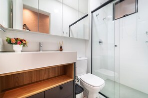 Un baño moderno con cabina de ducha de vidrio, un lavabo blanco con estante de madera y un inodoro.