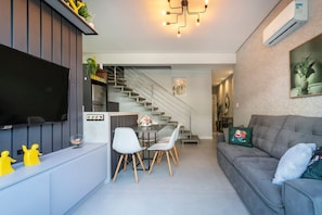 Un salon moderne doté d’un téléviseur à écran plat, d’un coin repas avec des chaises, d’un escalier et d’un canapé gris.