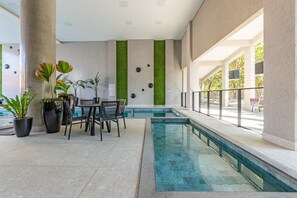 Un área de piscina interior moderna con zona de estar, detalles de pared verde y vistas despejadas al exterior.