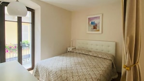 A bedroom with a bed, a nightstand, a window with a view, and a painting on the wall. - Appartamento Il Bottaio (Domodossola)