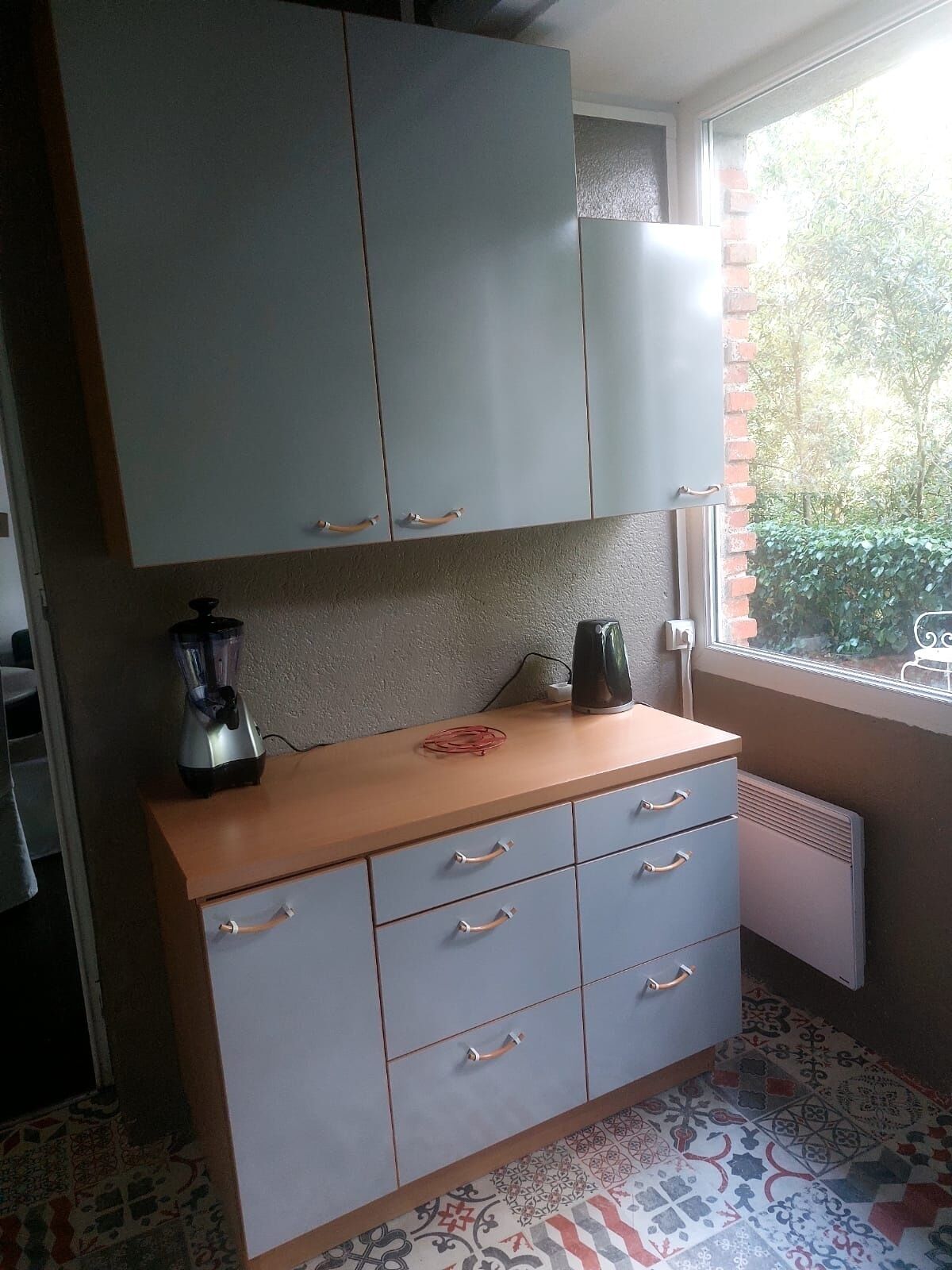 A compact kitchen with grey cabinets, a wooden countertop, and a patterned floor.