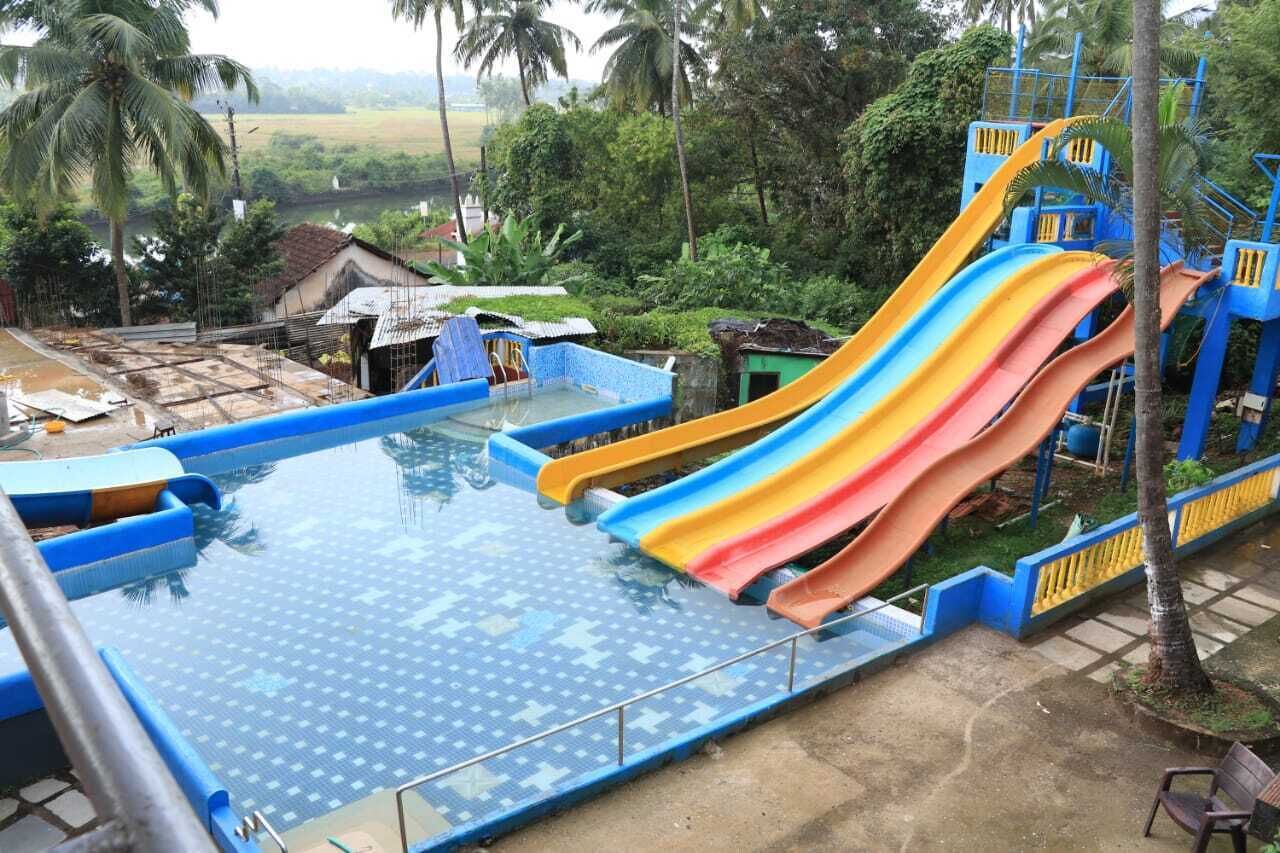 A swimming pool with multiple slides, surrounded by palm trees and a rural landscape.